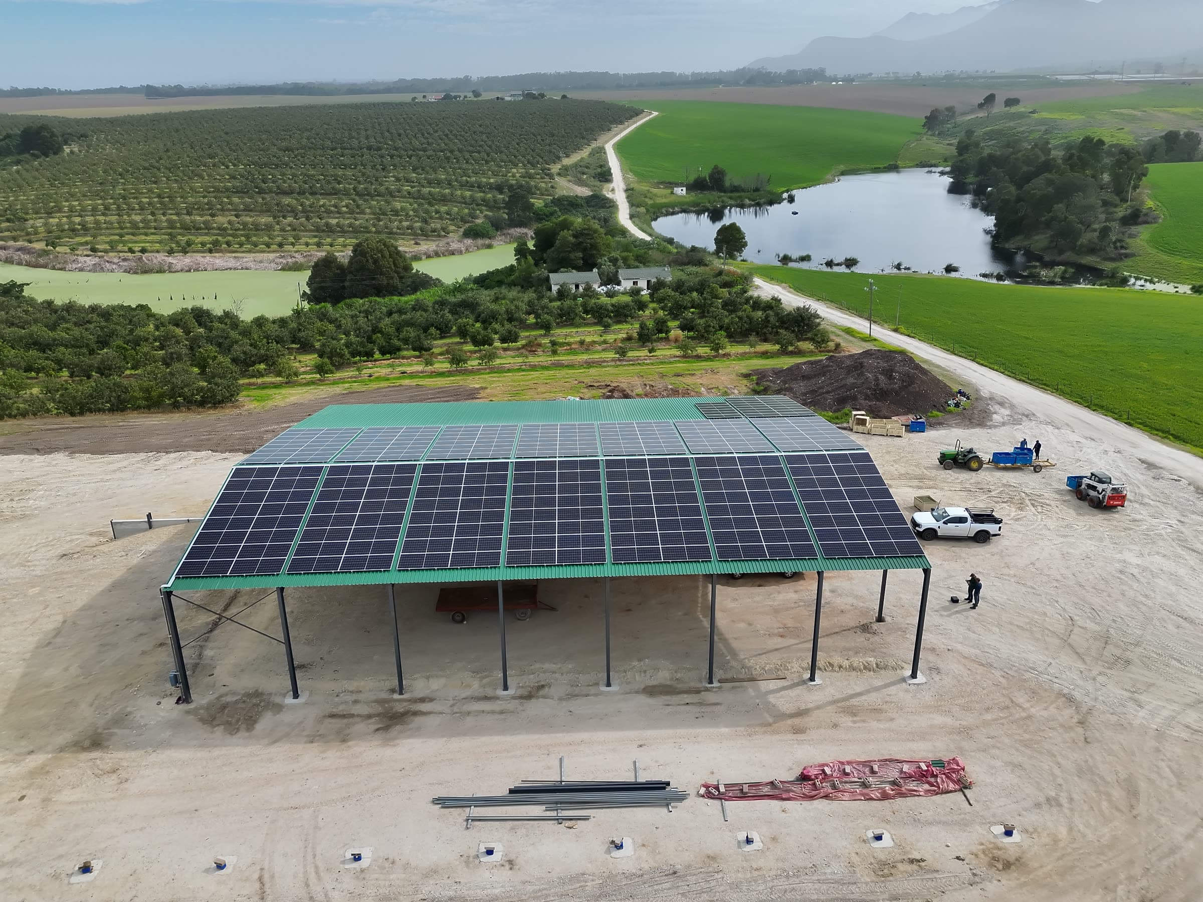 Solar PV canopy over an open-sided farm shed, orchards behind